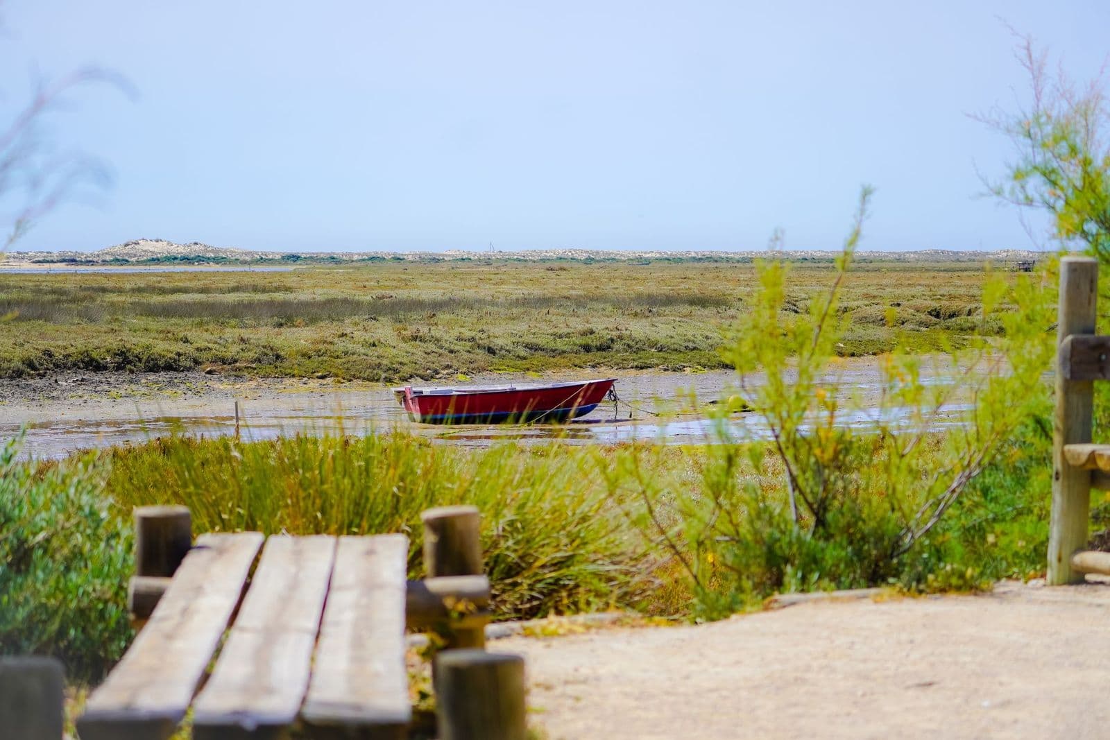Barque rouge échouée à marée basse au milieu des herbes d’une lagune, derrière un ponton en bois